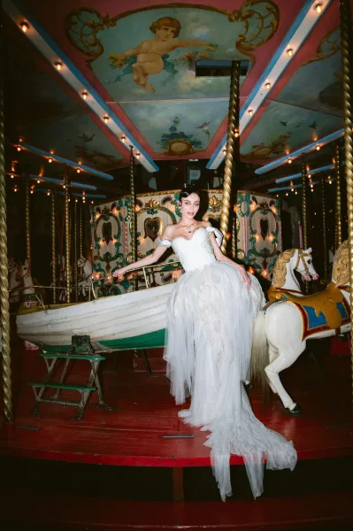 Bridal portrait of a bride on a vintage carousel, posing by a carousel horse in a tulle skirt beneath warm string lights.