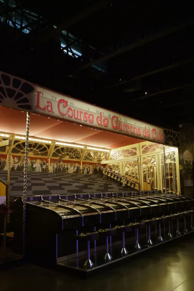 Carnival game booth styled as a vintage fairground attraction, crowned by a marquee sign beneath a dark, exposed-beam industrial ceiling.