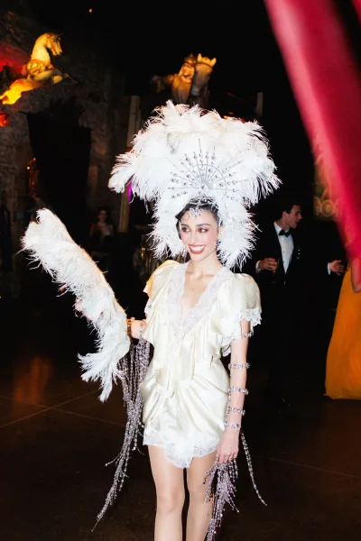 Wedding reception entertainment featuring a showgirl wedding performer twirling a feather fan amid black-tie guests in a dark, stone-walled venue.