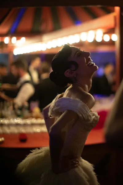 Bride dancing in a feather-trimmed gown, a candid reception party moment by the bar under warm string lights and a tent canopy.
