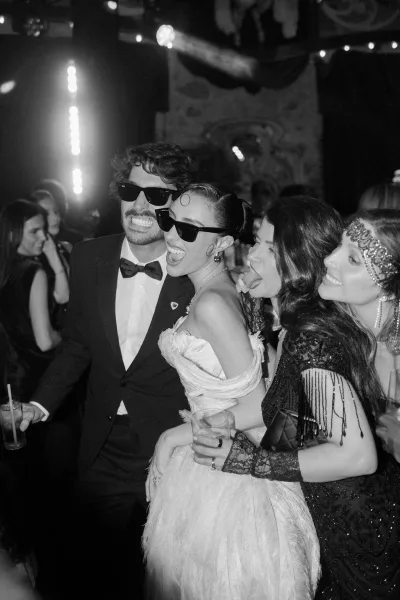 Reception dance floor alive at a wedding reception party as bride and groom in sunglasses, surrounded by guests and party lighting.