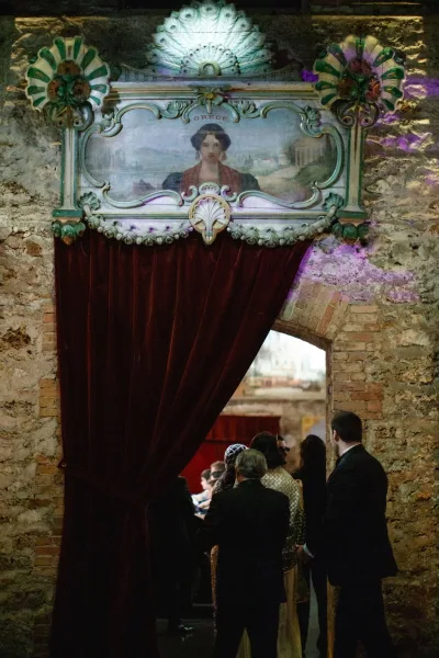 Wedding entrance decor with a velvet draped doorway set within a brick archway, framed by stone walls in an indoor venue.
