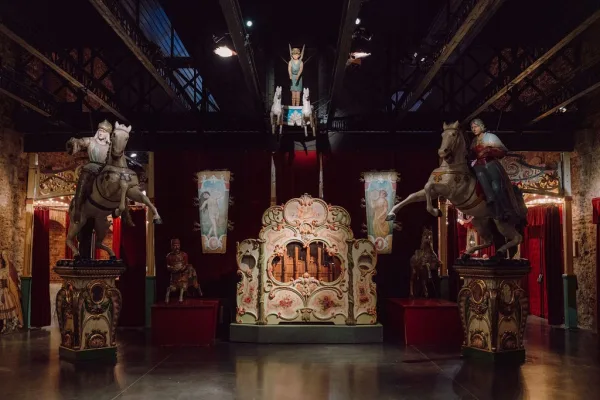 Carousel wedding venue framed by carousel horses beneath industrial ceiling beams and stone walls, set within a dark, polished concrete interior.