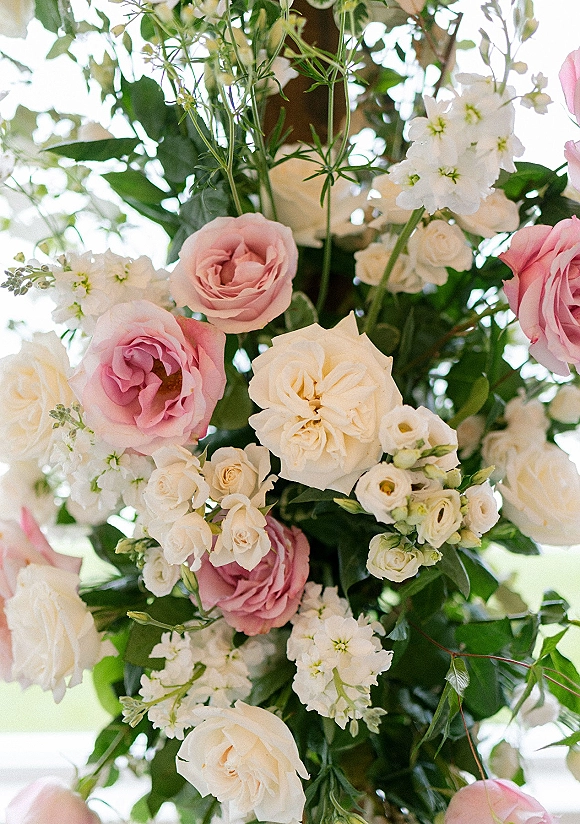 Wedding floral arrangement of pink and white wedding flowers with roses, spray roses, white stock, and greenery against blurred outdoor foliage