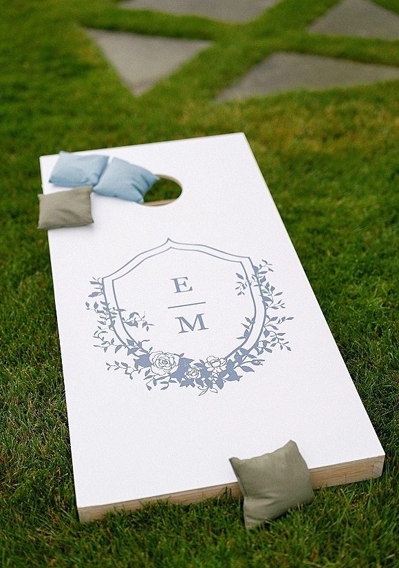 Wedding lawn games with wedding cornhole boards on a grass lawn, featuring a blue monogram decal and bean bags by stone pavers