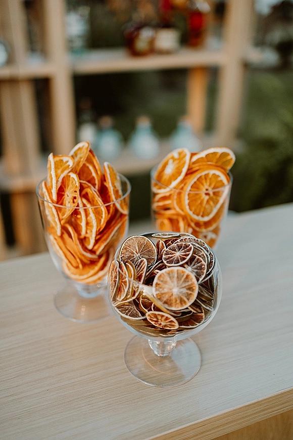 Dried citrus garnish with dried orange slices in glass bowls on a wooden tabletop, with window panes and blurred greenery behind