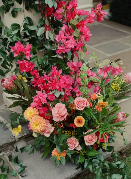 Wedding floral arrangement of bright wedding flowers with pink roses, coral dahlias, bougainvillea, and greenery on stone steps