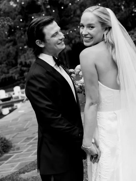 Couple portrait in a black and white wedding portrait style, bride smiling in a veil as groom admires her on a garden patio with lights