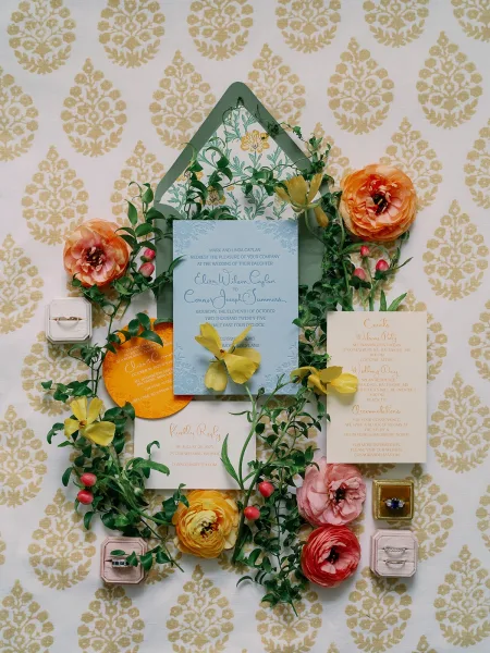 Invitation suite wedding invitation flat lay with blue calligraphy cards, wax seal, rings and ranunculus on patterned wallpaper background