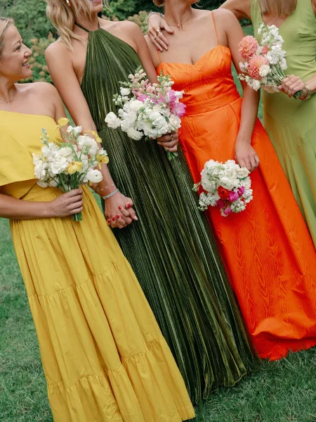 Bridesmaids dresses in mismatched bridesmaid dresses, with bouquets of colorful flowers, posed together on a green garden lawn