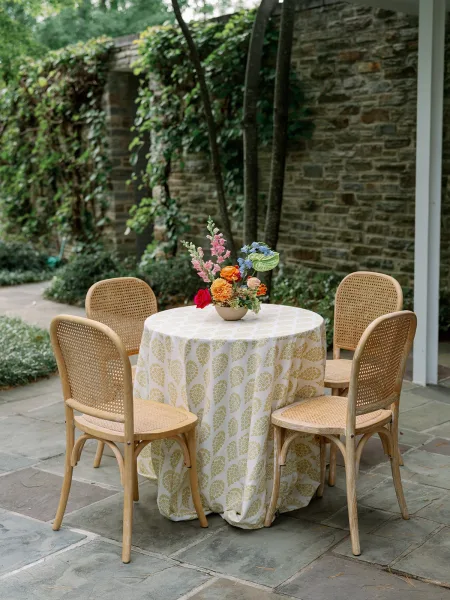 Reception tablescape with an outdoor wedding cocktail table, patterned cloth and colorful bowl-vase centerpiece on a stone patio courtyard with ivy wall