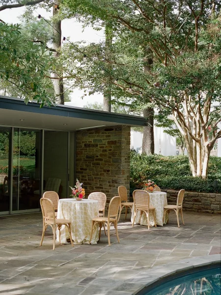 Outdoor reception seating with garden cocktail tables and round tables in rattan bistro chairs on a poolside stone patio under string lights