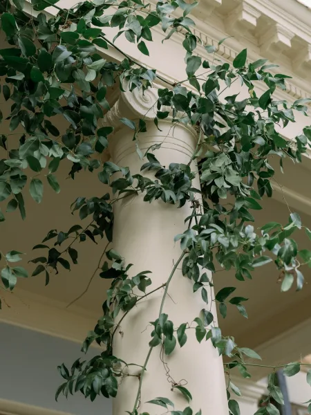 Wedding greenery decor with a greenery garland wedding decor wrapped around a white porch column, vine foliage draping beneath trim