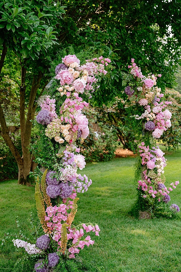 Wedding floral arch with peonies and roses, styled as an outdoor ceremony arch with vines and greenery on a garden lawn amid trees