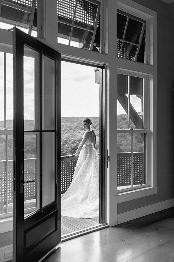 Bridal portrait in black and white of a bride looking over her shoulder in a strapless lace gown with long train by a doorway to a balcony