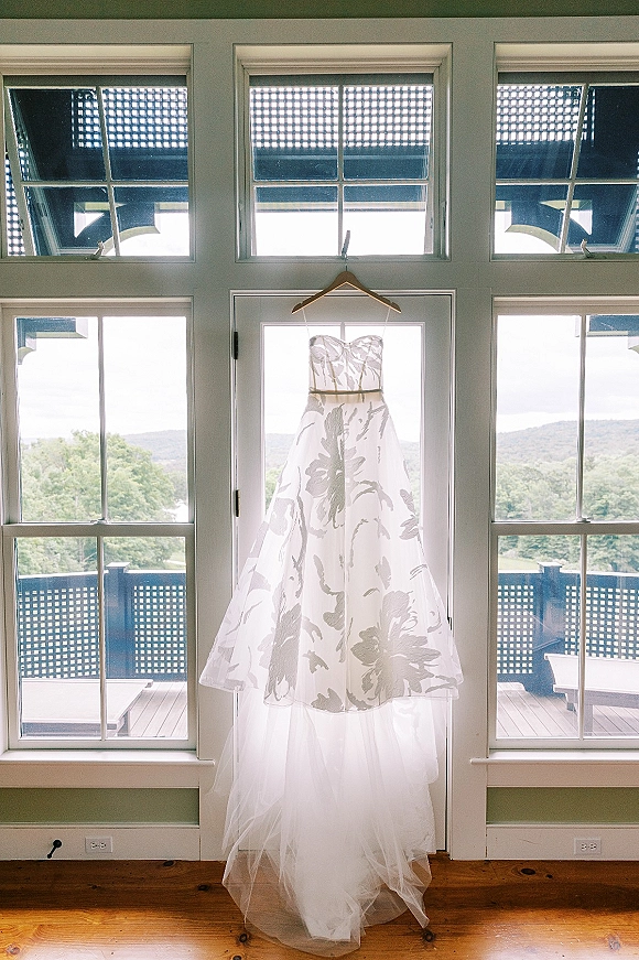 Wedding dress, strapless wedding dress with floral tulle skirt and sash belt on a wooden hanger by large windows and balcony railing