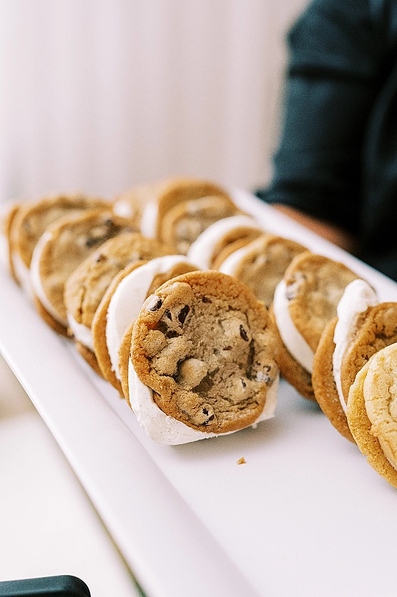 Ice cream sandwiches on a wedding dessert table arranged on a serving tray with vanilla filling, set on a white surface with blurred guest behind