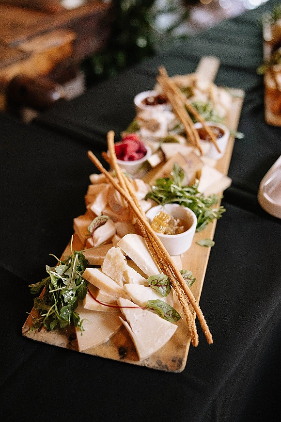 Wedding cheese board with assorted cheeses, crackers, breadsticks, nuts and jam ramekins, garnished with fresh herbs on a dark linen table
