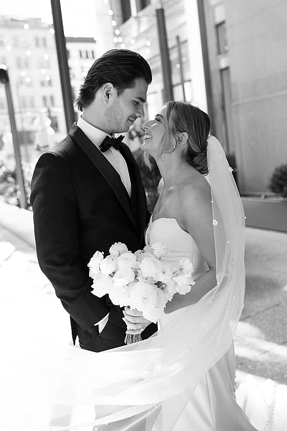Couple portrait in a black and white wedding portrait, bride and groom close up with veil and bouquet on a city street with string lights