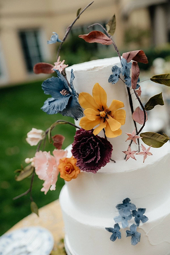 Wedding cake, two tier wedding cake with white buttercream frosting and sugar flowers, topped with branches on an outdoor lawn by windows