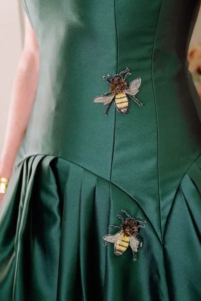 Wedding dress detail with bee appliqué, beadwork and embroidery on satin bodice, seam detailing sharp against blurred florals behind
