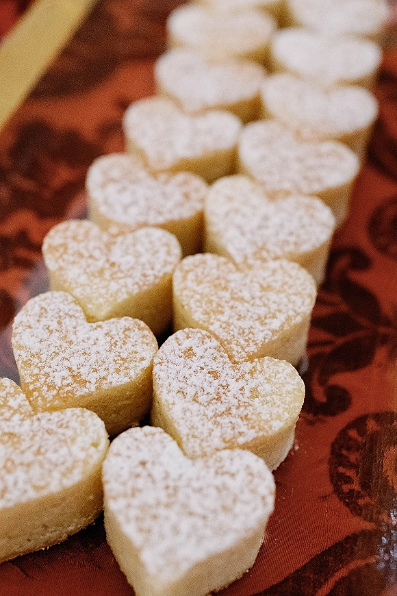 Wedding dessert of heart shaped wedding cookies dusted with powdered sugar on a red patterned tablecloth atop a table surface