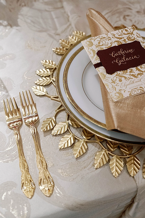 Wedding tablescape with gold wedding tablescape details, white and gold china, invitation and name card on a patterned tablecloth