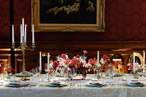 Reception tablescape with wedding table centerpiece, brass candelabras and taper candles, set with gold flatware against wood-paneled walls