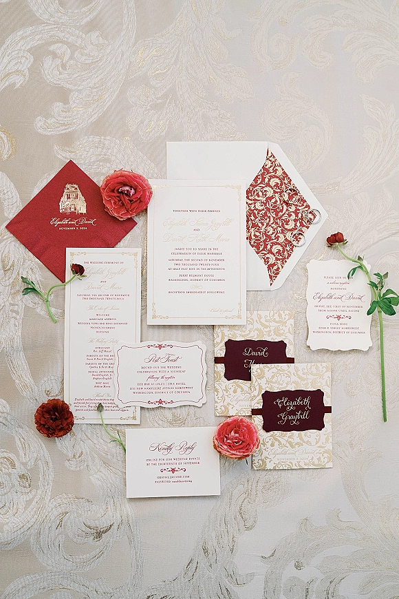 Wedding invitations suite with burgundy wedding invitations, wax seals, rings and floral accents arranged on a patterned fabric tablecloth