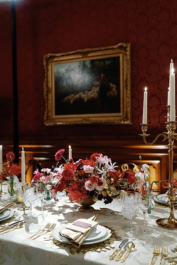Reception tablescape with a wedding floral centerpiece and taper candles in brass candelabra, set on linen with gold flatware and place cards