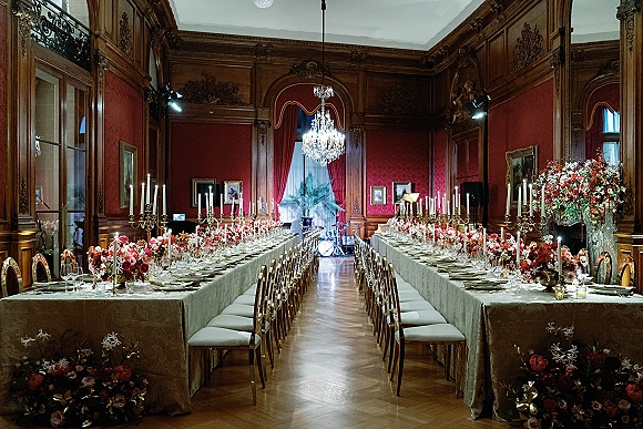 Reception tablescape with long banquet table wedding linens, lush florals and tall candelabras under chandelier in ornate wood-paneled room