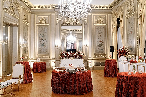 Wedding reception decor with red damask tablecloths, candlelit centerpieces, and chandelier glow in an ornate ballroom with gilded walls
