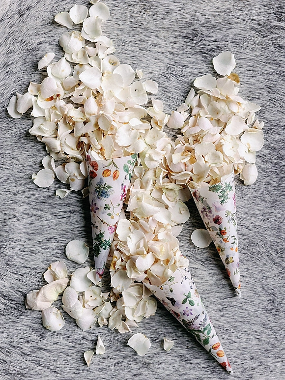 Flower petal confetti for a wedding petal toss in floral paper cones with white rose petals arranged on a gray faux fur rug