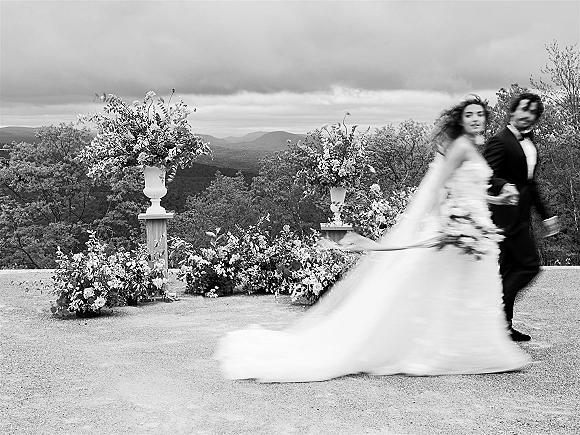 Couple portrait in a black and white wedding portrait, bride and groom walking hand in hand on a terrace with mountains behind