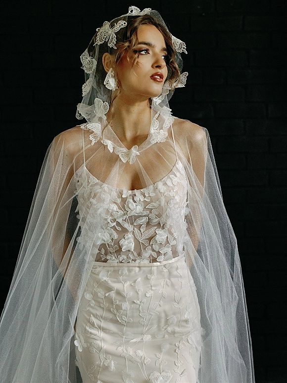 Bridal portrait of a bride in a lace veil, wearing a floral appliqué gown and red lipstick against a dark studio backdrop