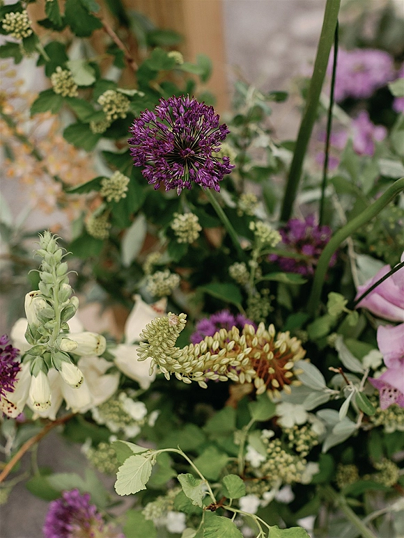 Wedding florals with purple allium blooms and white foxglove accents rising from lush greenery against softly blurred garden tones