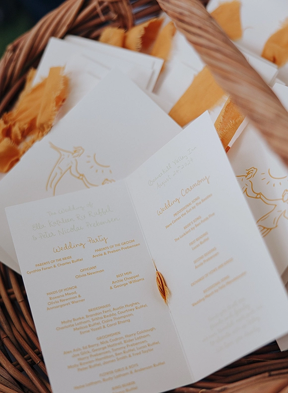 Wedding programs with ceremony program design in gold ink and tassel accents, neatly arranged in a woven basket with greenery