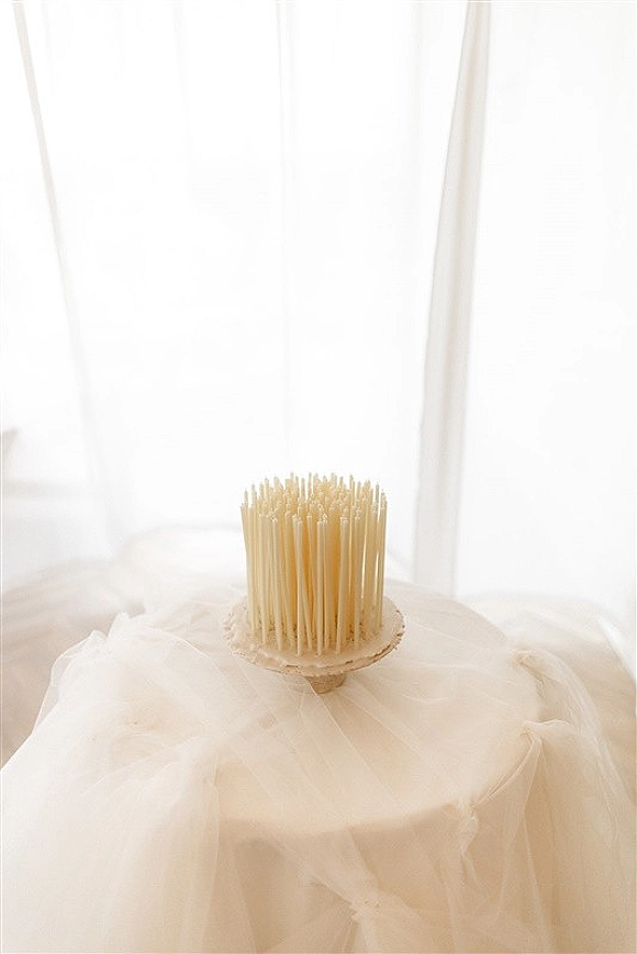 Cake pop display of wedding cake pops with white chocolate coating on a dessert stand, accented by tulle and sheer window-lit curtains