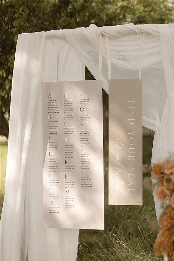 Wedding seating chart with alphabetical seating chart cards tied with ribbon and hung on white drapery, set outdoors on a green lawn