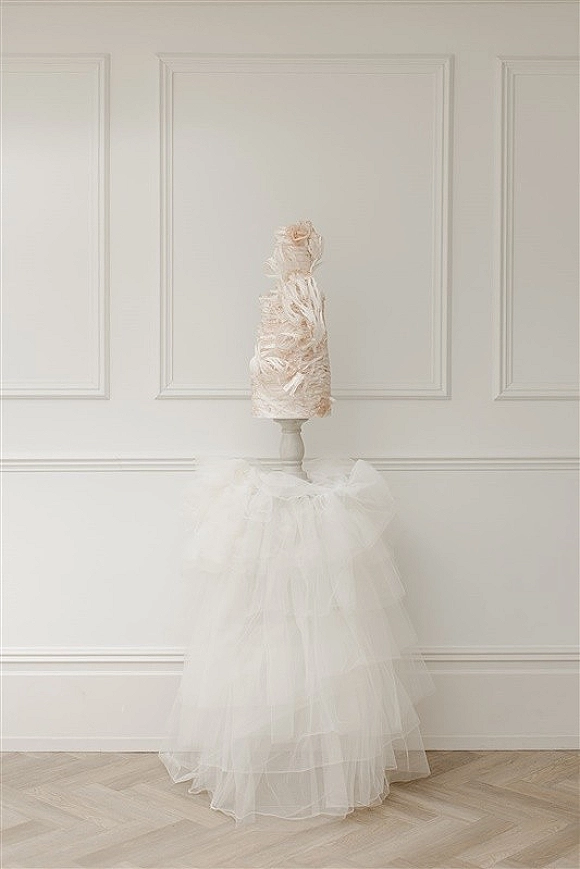 Bridal gown with a tulle wedding dress layered skirt displayed on a mannequin with a floral headpiece against a white paneled wall