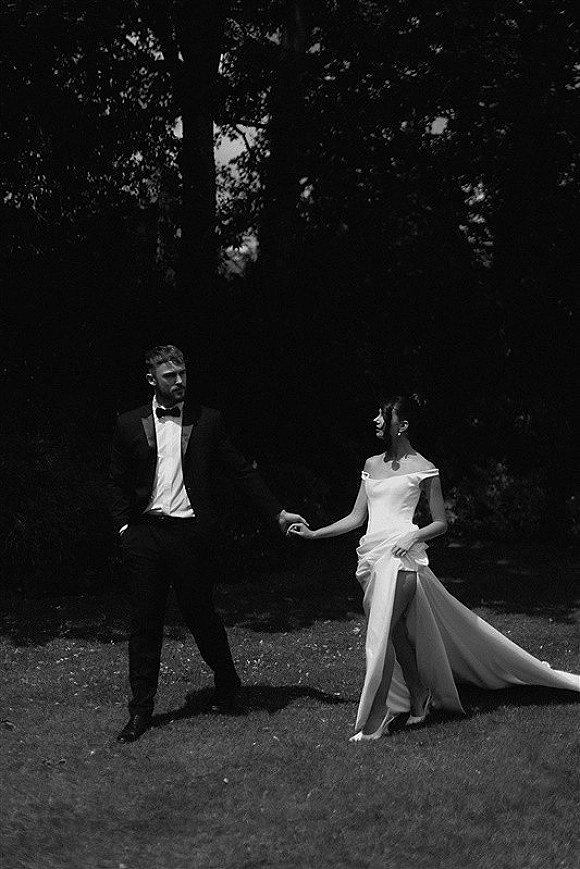 Couple portrait in a black and white wedding portrait style, bride and groom holding hands on a garden lawn under dappled tree shade