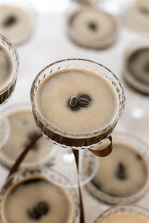 Espresso martini in coupe glasses with foam and coffee beans on a white tabletop, with other cocktails nearby for cocktail hour