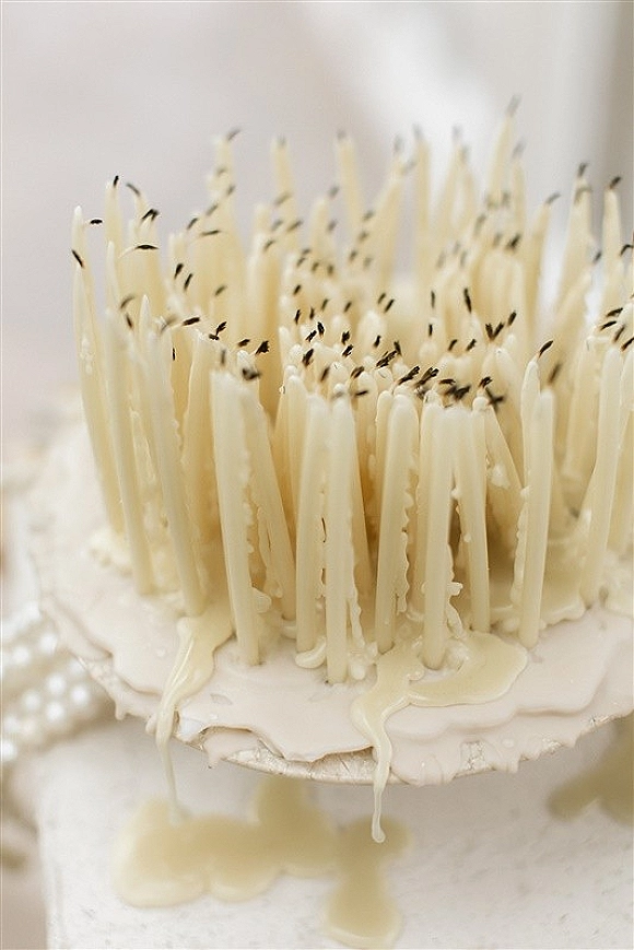 Wedding cake with candles, white frosting and melted wax drips on a cake stand against a clean white surface