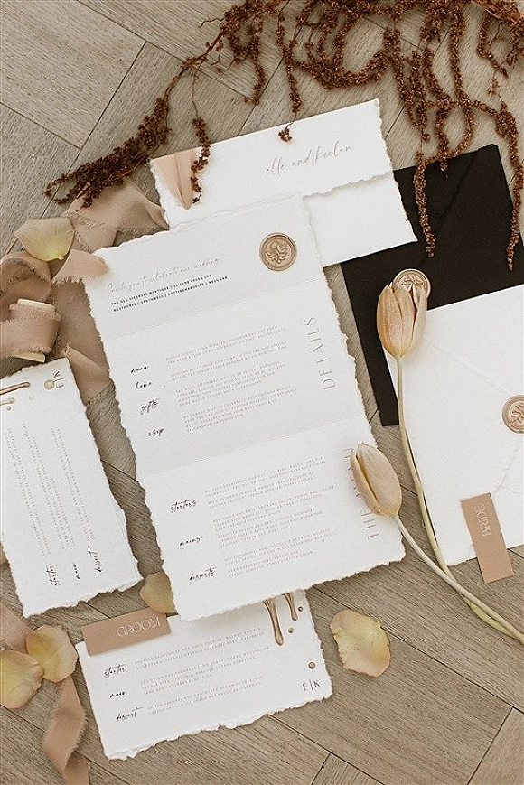 Invitation suite with deckle edge wedding invitations, wax seals, envelopes and tulips arranged in a flat lay on a wood floor