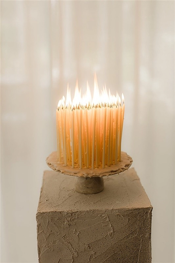 Wedding cake with tall candles on a pedestal stand, featuring textured buttercream icing against a white draped backdrop