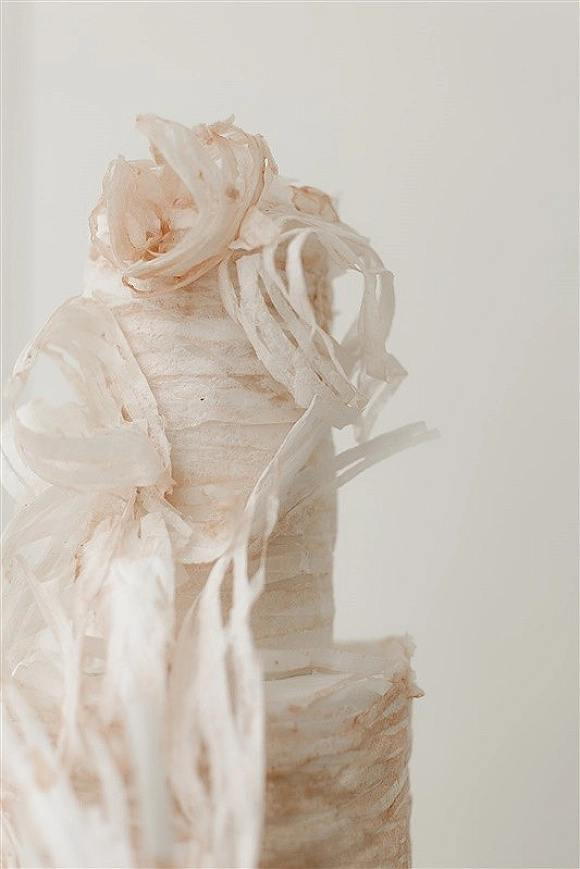 Wedding cake with white buttercream cake finish and wafer paper ruffles, sculptural tiers set against a clean white backdrop