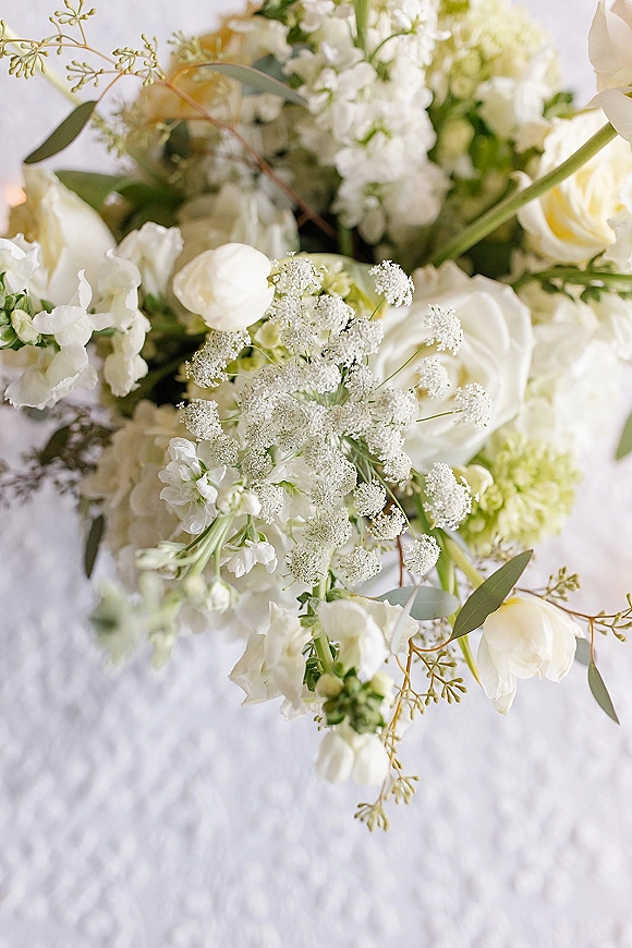 Wedding bouquet with white rose bouquet blooms, baby’s breath and greenery arranged on white textured fabric with eucalyptus accents