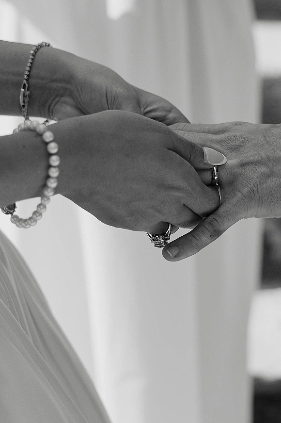 Wedding rings as a hand places a band beside an engagement ring, with a beaded bracelet and manicure in soft indoor light