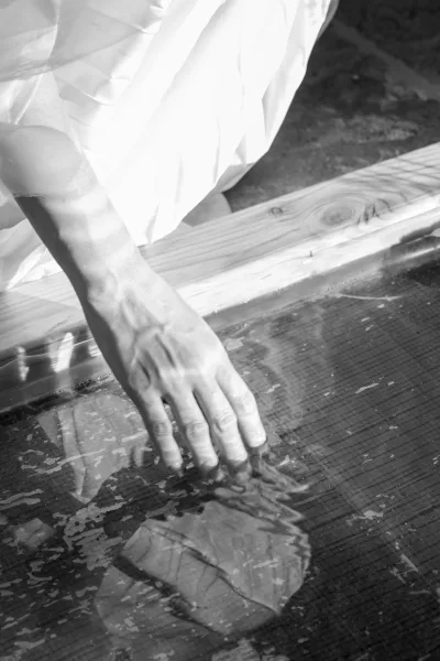 Bridal portrait detail in black and white, showing bride hand on glass with wedding dress fabric and veil reflected over wood floor
