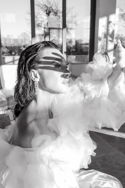 Bridal portrait in black and white of a bride in side profile wearing a ruffled tulle dress and crystal earrings by tall windows